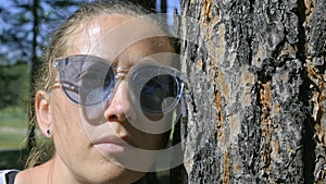 Portrait of a girl looking at the camera leaning against a tree trunk