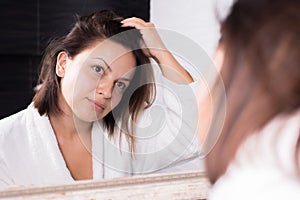 Portrait of a girl looking at herself in the reflection of the mirror, with disheveled hair. Greasy, dirty hair