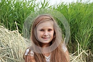 Portrait of a girl with loose hair sitting in the dry grass in nature