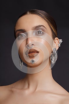 Portrait of a girl with makeup and jewelry applied to the face, posing with attitude, over gray background