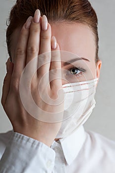 Portrait of a girl in a medical mask. I`ll cover one half of my face with my hand. Close up