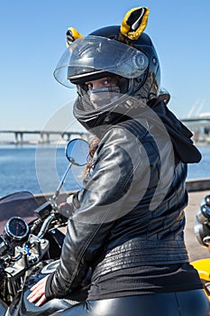 Portrait of girl motorcycle rider looking backward, sitting on a bike in black helmet with yellow ears