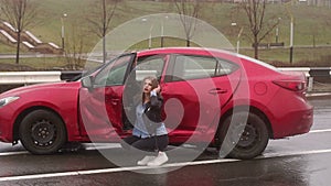 Portrait of a girl near her wrecked car after a severe accident on a wet road.