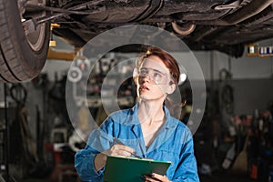 Portrait of a girl in overalls and glasses in a car repair shop. Blue overalls on a woman car mechanic. The concept of