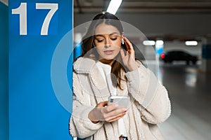 Portrait of girl with phone in hands who correcting the earphone in her ear. Young fashionable woman with phone and headphones