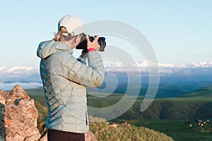 Portrait of a girl photographer in a cap on nature photographing on her digital mirror camera. Back view