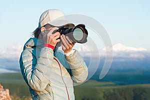 Portrait of a girl photographer in a cap on nature photographing on her digital mirror camera. Front view