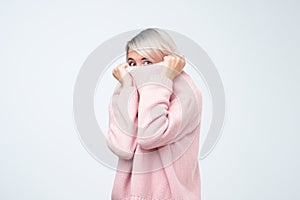 Portrait of girl pulling her pink sweater over head. Woman with scared look disappearing in her clothes