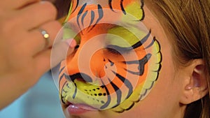Portrait girl receiving body art on face like tiger. Closeup tiger face aquagrum