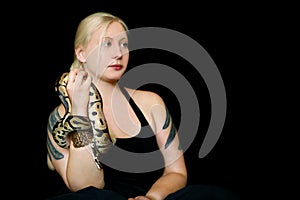 Portrait of girl with Royal Python snake. Woman holds snake in hands with beauty jewelry and posing in front of camera.