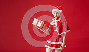 Portrait of a girl in a santa claus costume with a funny, dissatisfied grimace on her face with a gift in her hands on a red