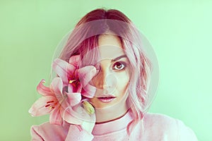 Portrait of girl with short wavy pink hair with pink flowers in her hair on green background