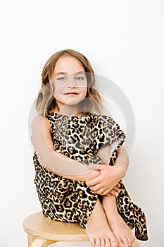 Portrait of a girl, she sits hugging her knees in a leopard print dress