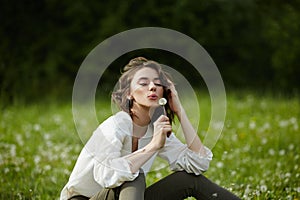 Portrait of a girl sitting in a field on the spring grass among dandelion flowers. Cheerful girl enjoys Sunny spring weather.