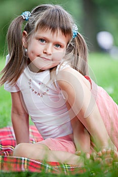 Portrait of girl sitting on plaid, grass in park