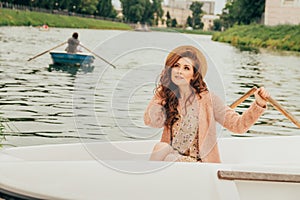portrait girl is sitting in a white boat on the river. in the distance one sees a retiring boat with a rower