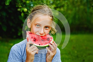 Portrait of a girl with a slice of watermelon in nature on a background of greenery. The child bites off a piece of red watermelon