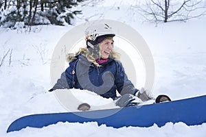 Portrait of a girl snowboarder in the snow. A girl in a ski helmet and a jacket lies on the snow