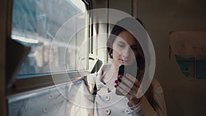 Portrait of girl standing in the train and using smartphone. Young woman texting sms and browse the Internet.