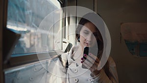 Portrait of girl standing in the train and using smartphone. Young woman texting sms and browse the Internet.