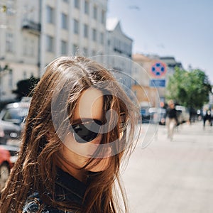 Portrait of a girl with sunglasses against the background of the city with flying hair in the wind