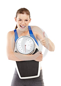 Portrait of girl, thumbs up and scale for weight loss in studio, measurement and results of fitness goal. Female person