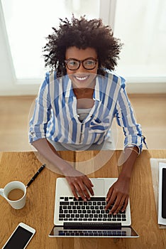 Portrait, girl and top view with laptop, working and home with coffee, remote work and smile. African woman, typing and