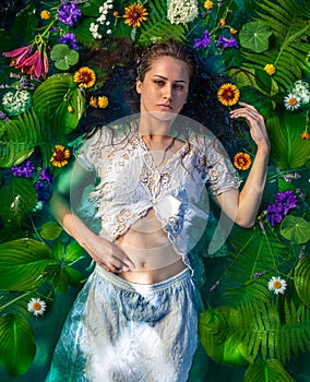 Portrait of a girl in water with flowers and green leaves