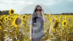 Portrait of girl wearing sunglasses, standing in sunflower field among flowers