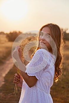 Portrait of a girl in a white dress in the rays of the sunset backlight of the summer sun