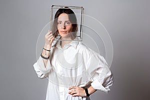 Portrait of a girl in a white shirt with a metal cube-cage on his head. isolate. The concept of estrangement, the man in a case