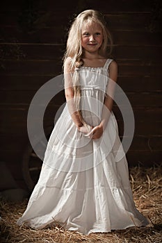 Portrait of a girl in a white sundress on the hay in the barn