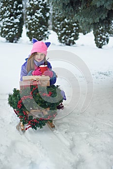 Portrait of girl in winter forest. Girl carries a Christmas tree and presents with sled.