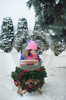 Portrait of girl in winter forest. Girl carries a Christmas tree and presents with sled.