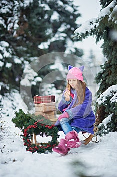 Portrait of girl in winter forest. Girl carries a Christmas tree and presents with sled.