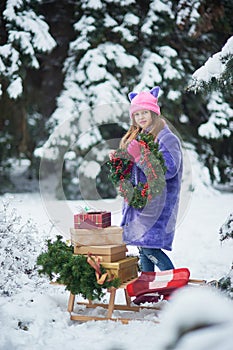 Portrait of girl in winter forest. Girl carries a Christmas tree and presents with sled.