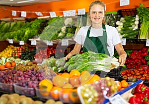 Portrait of a girl working part-time as a trainee seller, holding a crate of precocious Chinese cabbage