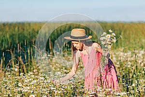 Portrait of girl in a yellow dress and straw hat on a chamomile field in summer