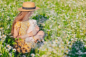 Portrait of girl in a yellow dress and straw hat on a chamomile field in summer