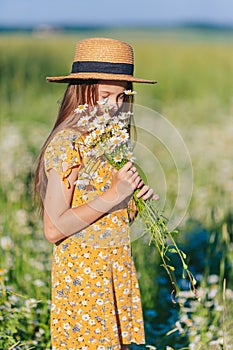 Portrait of girl in a yellow dress and straw hat on a chamomile field in summer