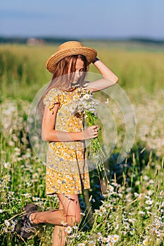 Portrait of girl in a yellow dress and straw hat on a chamomile field in summer