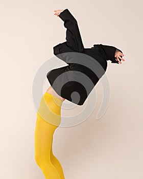 Portrait of girl in yellow tights posing tangled up in black jacket isolated over grey studio background