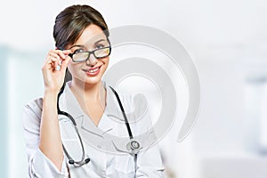 Portrait of glad smiling doctor in white uniform standing with crossed hands on blue clinic background