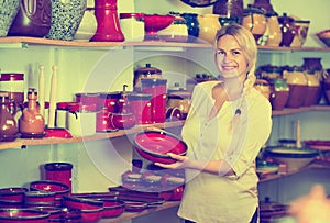 Portrait of glad woman choosing glazed with red color ceramic ut