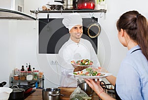 Man cook giving to waitress ready to serve salad