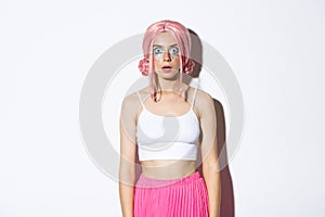 Portrait of glamorous party girl in pink wig and bright makeup, drop jaw and looking startled at camera, stare at