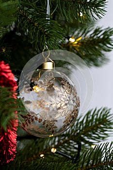 A portrait of a glass christmas ball decorated with gold and diamonds hanging from a christmas tree together with other holiday