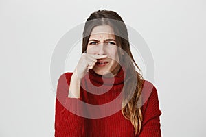 Portrait of gloomy attractive european girl with rainy nose holding her index finger under nose, isolated over white