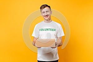 Portrait of good kind man in white t-shirt with written inscription green title volunteer with blank cardboard box