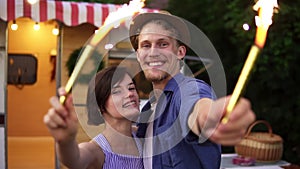 Portrait of a good looking couple embracing standing with sparklers celebrating, waving hands with fireworks sticks